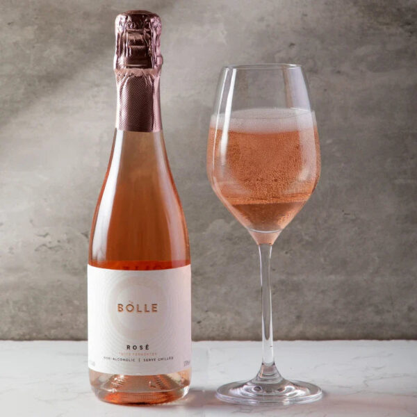 Flaska af BOLLE Sparkling Rosé og glas með ljósbleiku freyðivíni við ljósan steinvegg