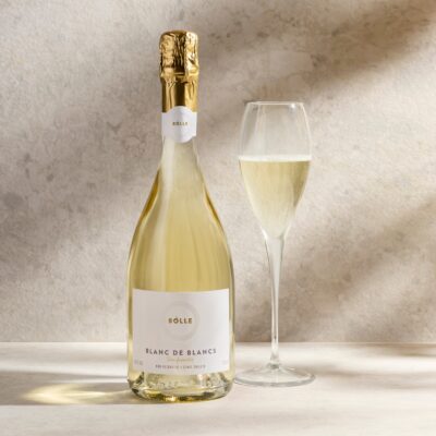 Flaska af BOLLE Blanc de Blancs og glas með ljósgylltu freyðivíni við ljósan steinvegg
