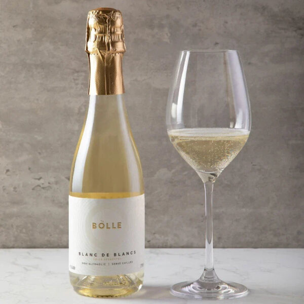 Flaska af BOLLE Blanc de Blancs og glas með ljósgylltu freyðivíni við ljósan steinvegg