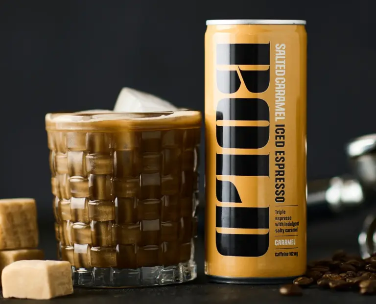Dós af BOLD Salted Caramel Iced Espresso og ískaffi með klökum í glasi við karamellubita