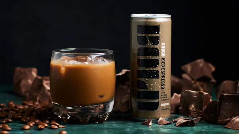Dós af BOLD Choco Iced Espresso og ískaffi í glasi innan um súkkulaðibita og kaffibaunir