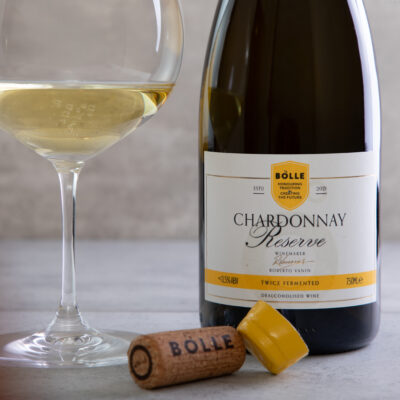 Flaska af BOLLE Chardonnay Reserve, korktappi og glas með hvítvíni á ljósum steini