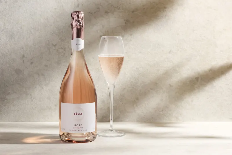 Flaska af BOLLE Sparkling Rosé og fullt glas á ljósum steini í síðdegisbirtu