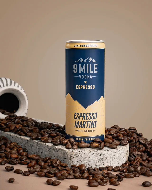 Dós af 9 MILE Espresso Martini með fjallatindum á miðanum, á steini innan um kaffibaunir